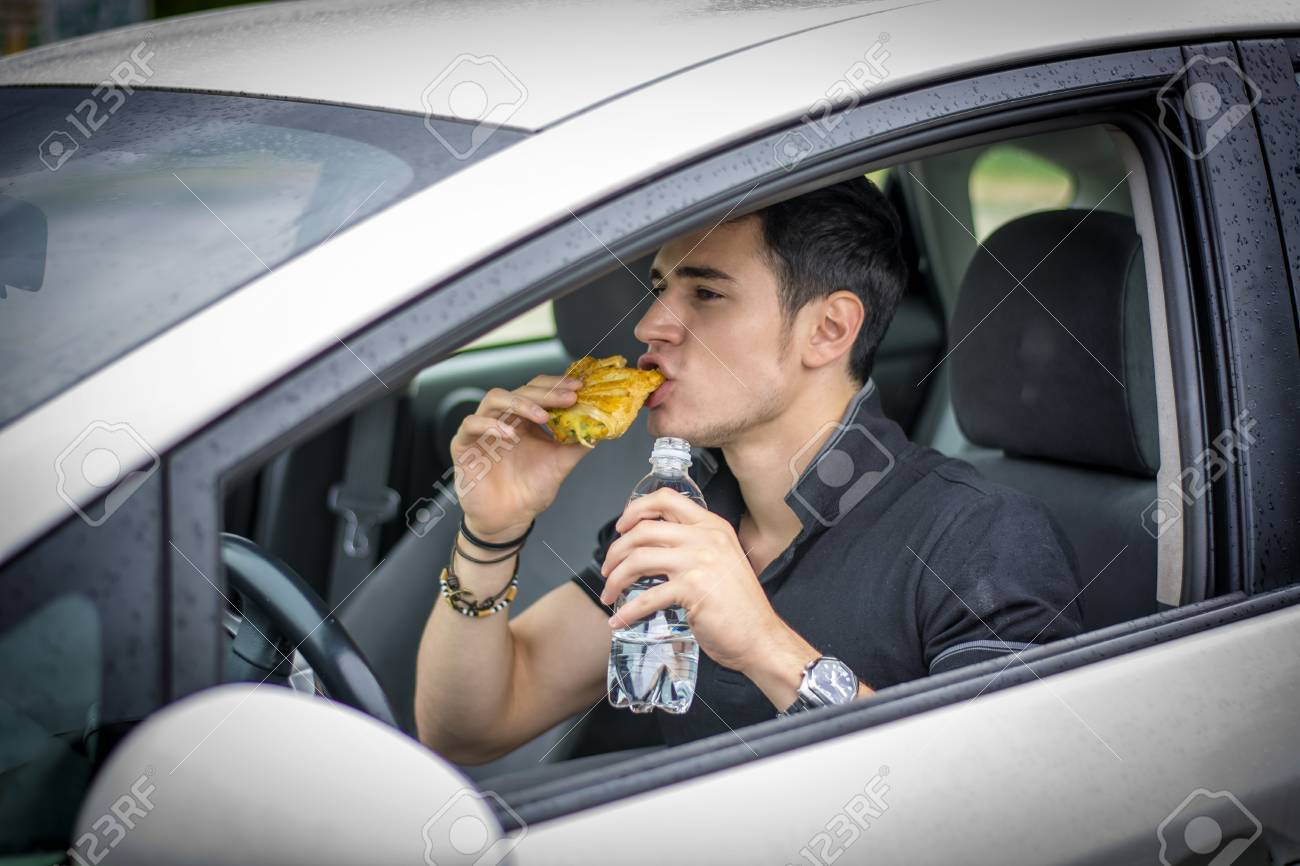 彼の車を運転して交通の食品を食べながら若いハンサムな男 の写真素材 画像素材 Image