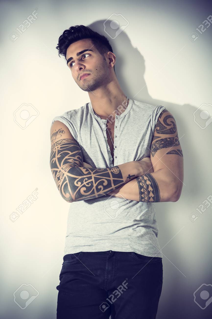 Handsome Tattooed Young Man Wearing Grey T-shirt, Standing Against Light  Background In Studio Shot With Arms Crossed On Chest Stock Photo, Picture  and Royalty Free Image. Image 76128633., image size:866x1300