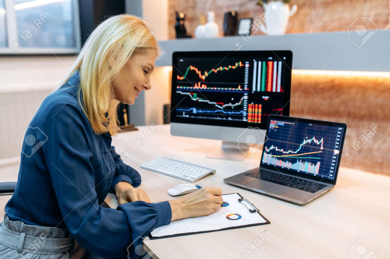 Successful Smart Mature Woman Investor And Crypto Trader, Using Pc And  Laptop, Analyzes Charts Of Trading In Stock Market And Digital  Cryptocurrency Exchange, Conducts Analysis, Trading Crypto Coins Stock  Photo, Picture and