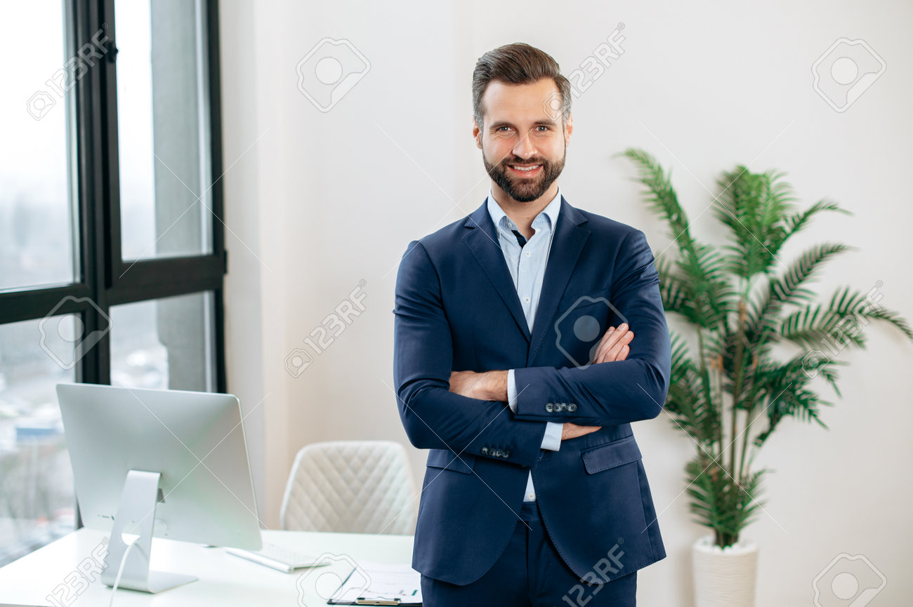 Portret przystojnego, pewnego, eleganckiego, odnoszącego sukcesy brodatego mężczyzny rasy kaukaskiej, w garniturze, top manager, dyrektor generalny firmy, dyrektor finansowy, stoi w biurze, ze skrzyżowanymi rękami, patrząc w kamerę, uśmiechając się - 191820015 Portret przystojnego, pewnego, eleganckiego, odnoszącego sukcesy brodatego mężczyzny rasy kaukaskiej, w garniturze, top manager, dyrektor generalny firmy, dyrektor finansowy, stoi w biurze, ze skrzyżowanymi rękami, patrząc w kamerę, uśmiechając się - 191820015