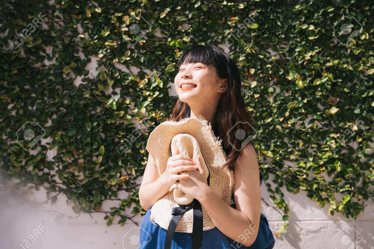 Portrait of young asian woman traveler wearing blue dress holding straw hat over nature background. - 155420324 Portrait of young asian woman traveler wearing blue dress holding straw hat over nature background. - 155420324