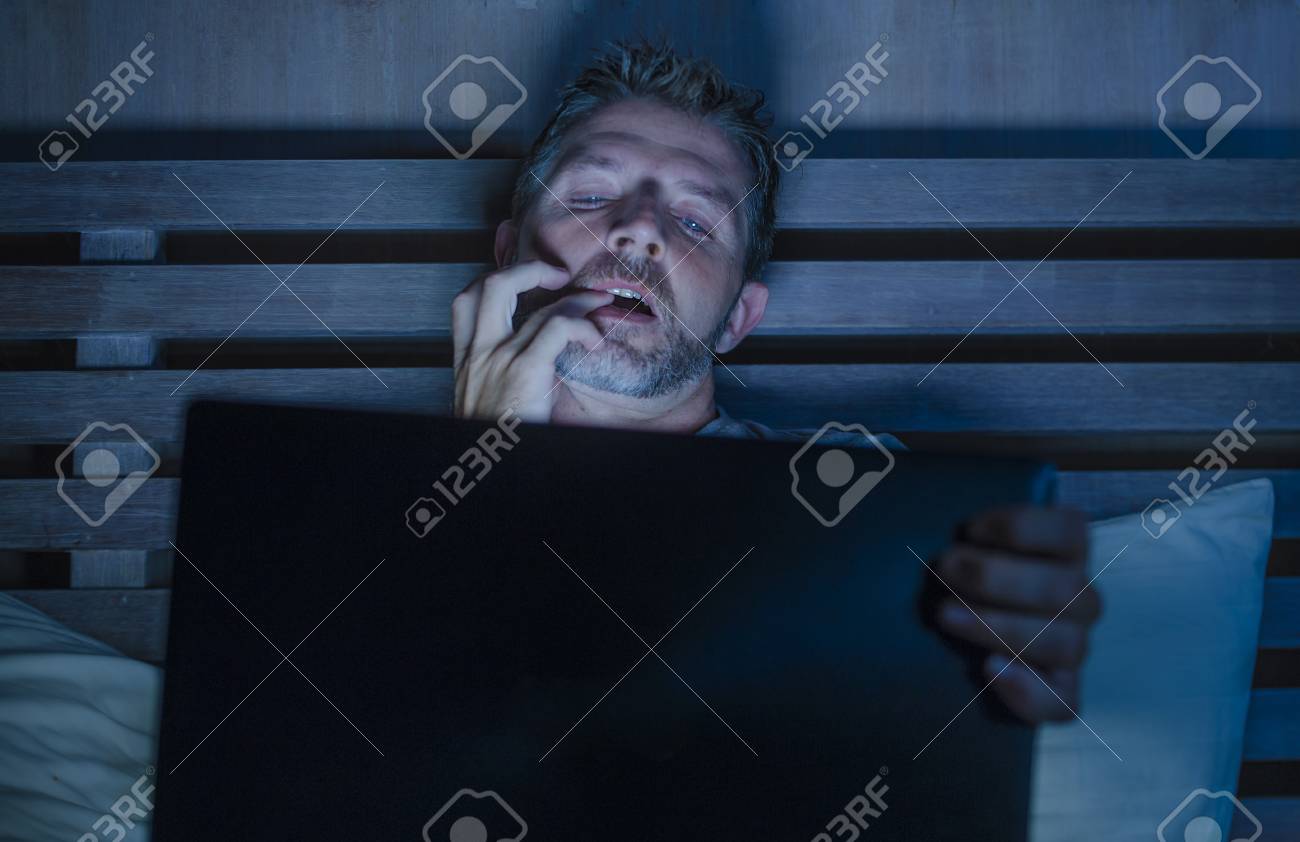 Young Aroused Man Alone In Bed Playing Cybersex Using Laptop Computer  Watching Porn Sex Movie Late At Night With Lascivious Pervert Face  Expression In Internet Pornographic Sexual Content Stock Photo, Picture and