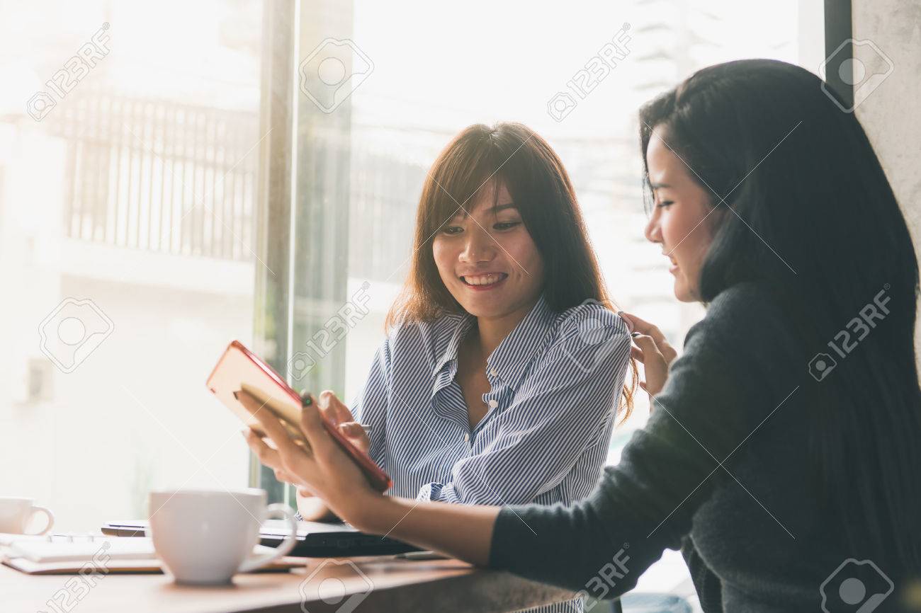 一対一の会議 カフェのテーブルに座っている 2 人の若いビジネス女性 女の子は ノート パソコンの画面に同僚の情報を示しています スマート フォン ブログの使用女の子 チームワークのビジネスミーティング労働者やフリーランサー の写真素材 画像素材 Image