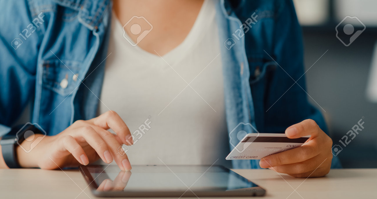 Young asia lady using tablet order online shopping product and paying bills with credit card in living room interior. Stay at house, Self quarantine activity, Fun activity for coronavirus prevention. - 169421872 Young asia lady using tablet order online shopping product and paying bills with credit card in living room interior. Stay at house, Self quarantine activity, Fun activity for coronavirus prevention. - 169421872