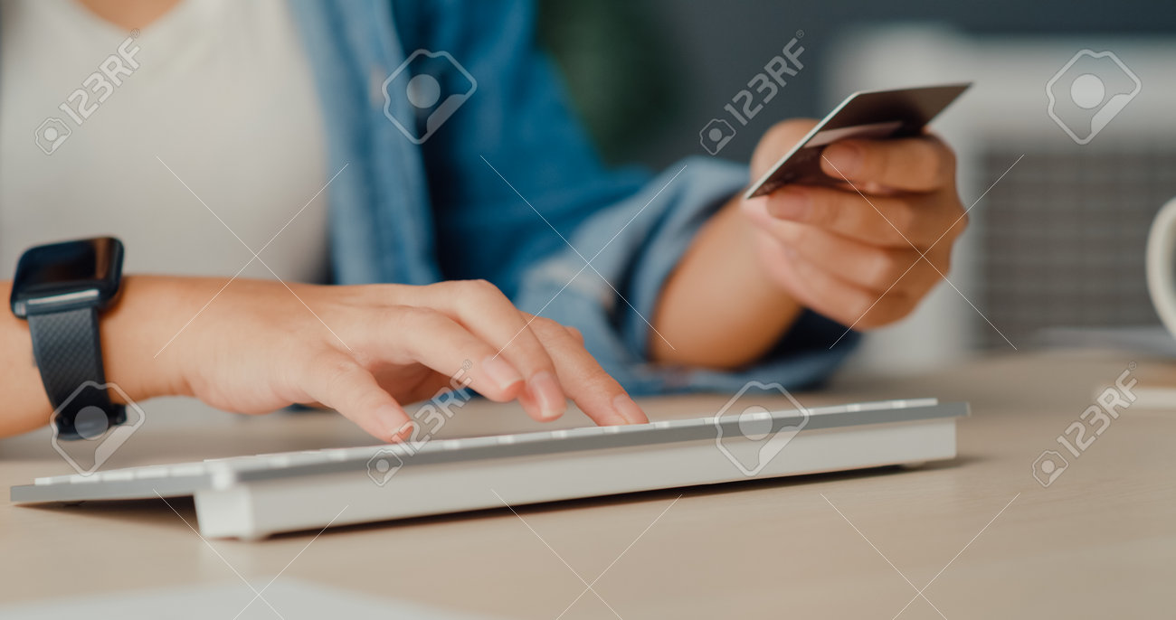 Young asia lady using computer order online shopping product and paying bill with credit card in living room interior. Stay at house, Self quarantine activity, Fun activity for coronavirus prevention. - 169421873 Young asia lady using computer order online shopping product and paying bill with credit card in living room interior. Stay at house, Self quarantine activity, Fun activity for coronavirus prevention. - 169421873