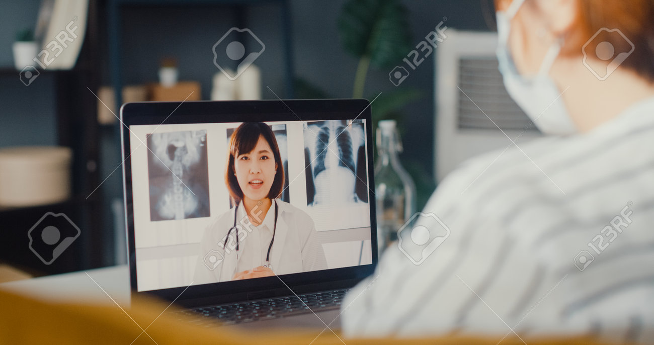 Young Asia girl using computer laptop talk about disease in video conference call with senior doctor online consultation in living room at house. Social distancing, quarantine for coronavirus concept. - 169422867 Young Asia girl using computer laptop talk about disease in video conference call with senior doctor online consultation in living room at house. Social distancing, quarantine for coronavirus concept. - 169422867