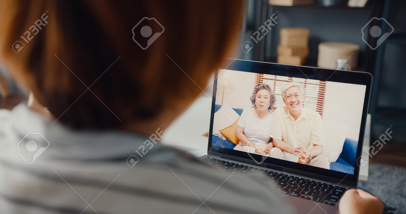 Young Asia girl using laptop video call meeting talk with elderly family dad and mom while work from home sitting on sofa at living room. Social distancing, quarantine for corona virus prevention. - 169422874 Young Asia girl using laptop video call meeting talk with elderly family dad and mom while work from home sitting on sofa at living room. Social distancing, quarantine for corona virus prevention. - 169422874