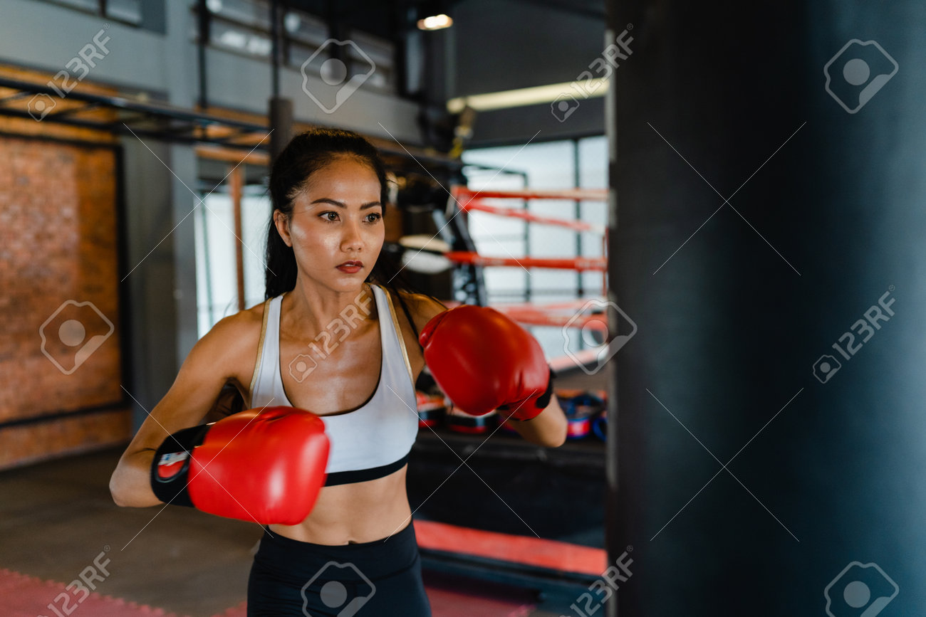 Young Asia lady kickboxing exercise workout punching bag tough female fighter practice boxing in gym fitness class. Sportswoman recreational activity, functional training, healthy lifestyle concept. - 169422987 Young Asia lady kickboxing exercise workout punching bag tough female fighter practice boxing in gym fitness class. Sportswoman recreational activity, functional training, healthy lifestyle concept. - 169422987