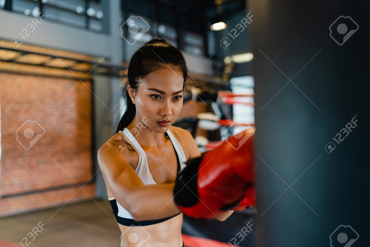 Young Asia lady kickboxing exercise workout punching bag tough female fighter practice boxing in gym fitness class. Sportswoman recreational activity, functional training, healthy lifestyle concept. - 169422992 Young Asia lady kickboxing exercise workout punching bag tough female fighter practice boxing in gym fitness class. Sportswoman recreational activity, functional training, healthy lifestyle concept. - 169422992