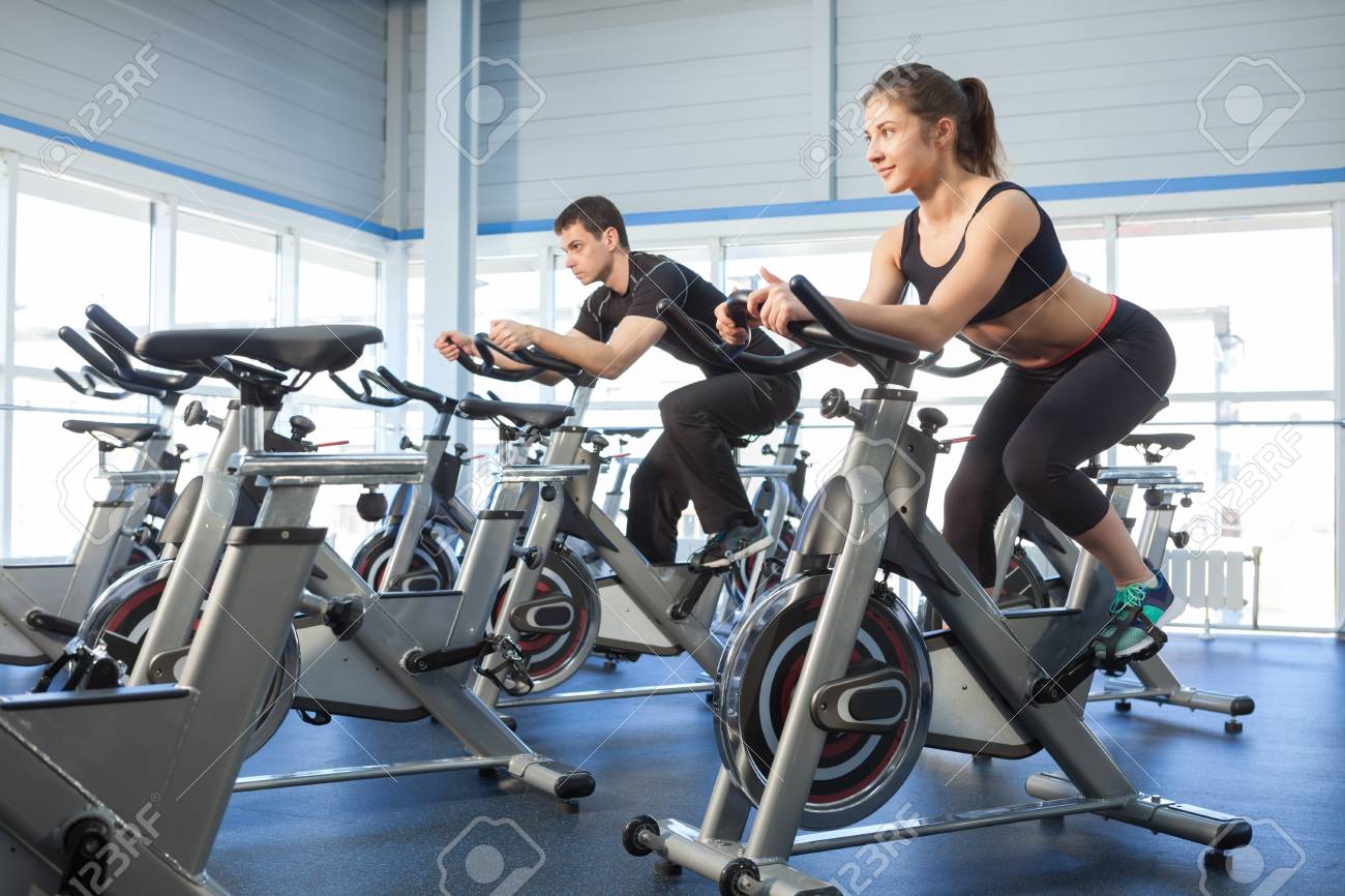Man And Woman Using Cycling Exercise Bikes At The Gym Stock Photo, Picture  And Royalty Free Image. Image 56641588.