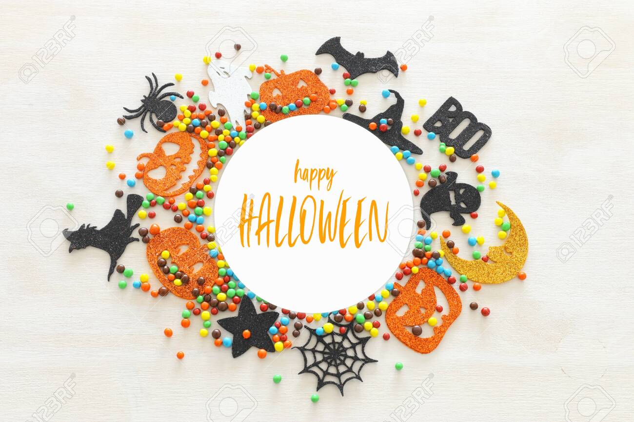 holidays image of Halloween. Pumpkins, bats, treats, bat and witch over white wooden background. top view, flat lay - 128926081 holidays image of Halloween. Pumpkins, bats, treats, bat and witch over white wooden background. top view, flat lay - 128926081