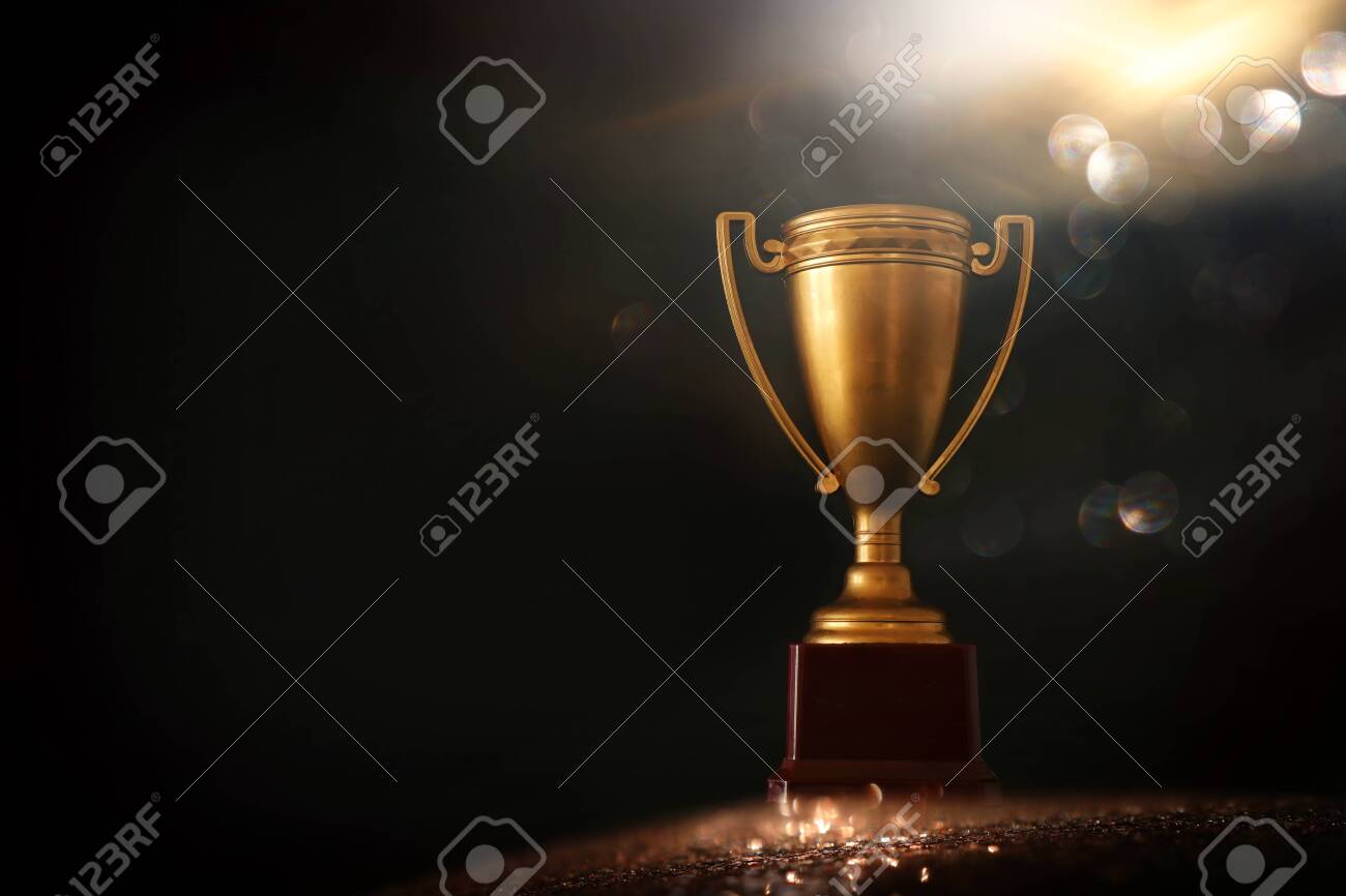 low key image of trophy over wooden table and dark background, with abstract shiny lights - 137390466 low key image of trophy over wooden table and dark background, with abstract shiny lights - 137390466