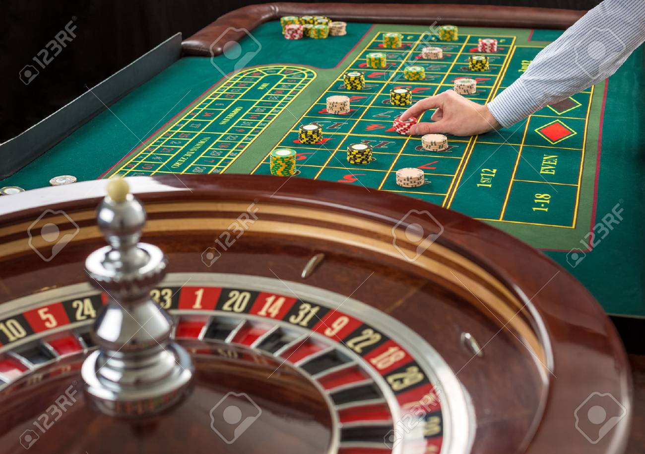 Nahaufnahme von Roulette und Haufen von Spielmarken auf einem grünen Tisch im Casino. Man Hand über Casino Chips auf Roulette Tisch Nahaufnahme von Roulette und Haufen von Spielmarken auf einem grünen Tisch im Casino. Man Hand über Casino Chips auf Roulette Tisch