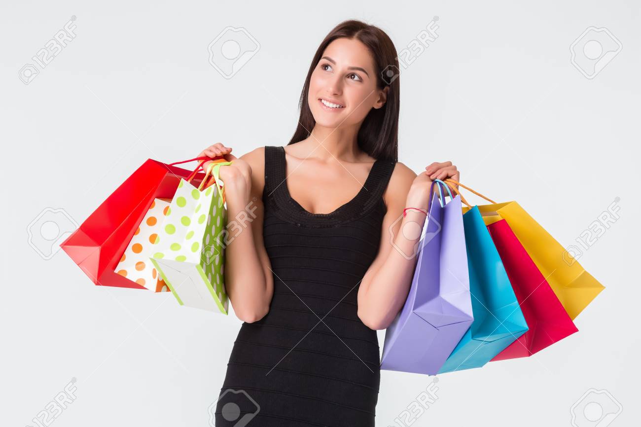 Feliz sonriente mujer joven con bolsas de compras después de ir de compras. La morena en un vestido negro, aislado en fondo blanco Feliz sonriente mujer joven con bolsas de compras después de ir de compras. La morena en un vestido negro, aislado en fondo blanco