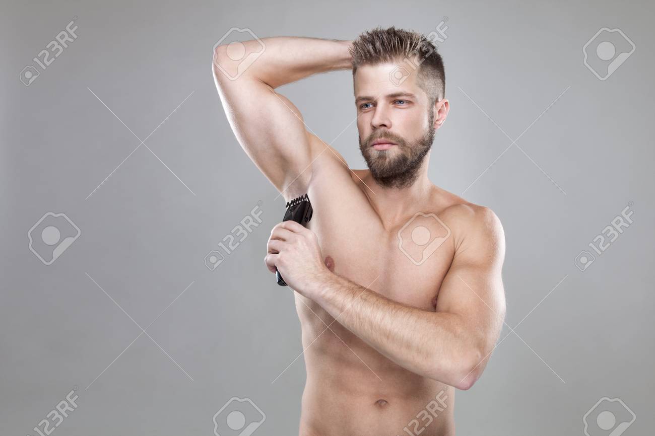 Handsome Young Bearded Man With A Trimmer Shaving Off Body Hair
