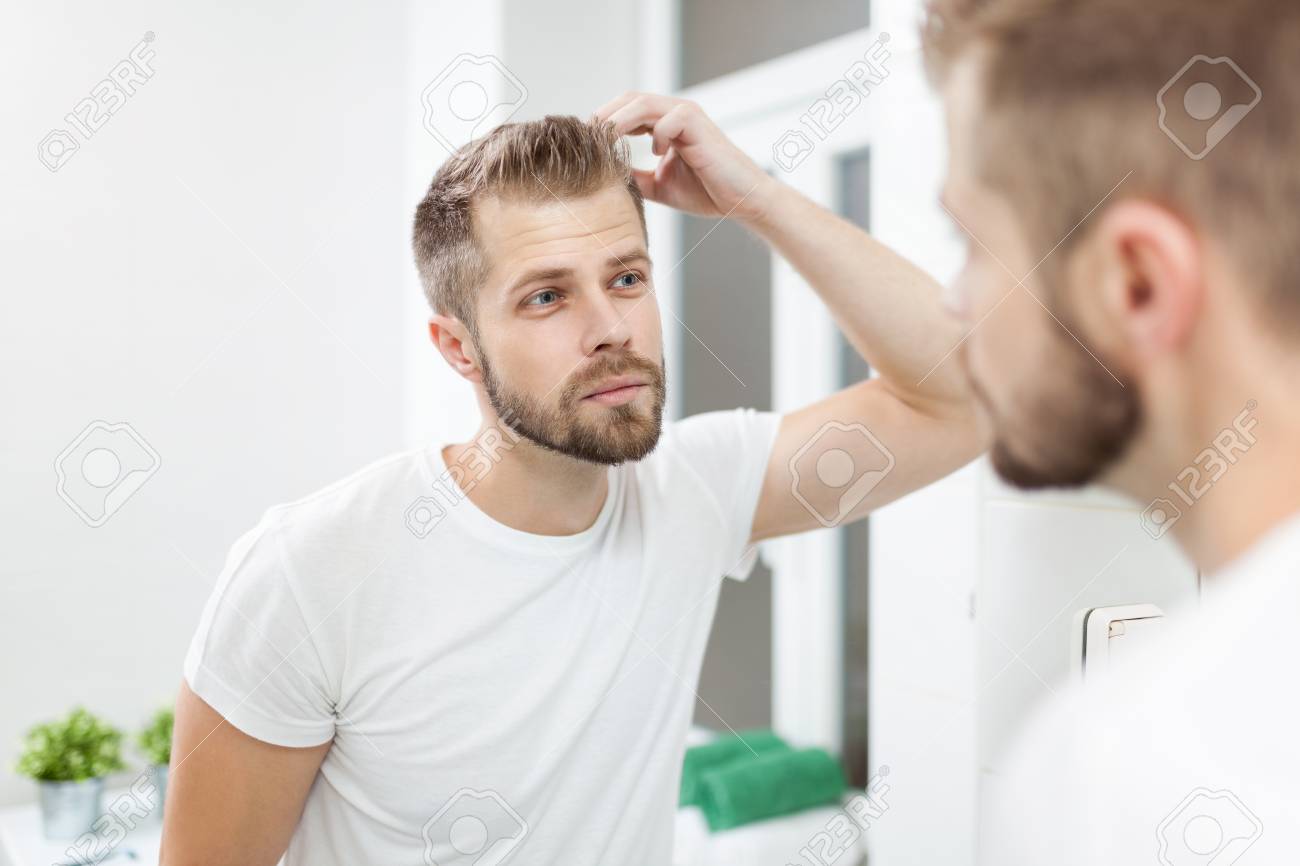 handsome unshaven man looking into the mirror in bathroom stock