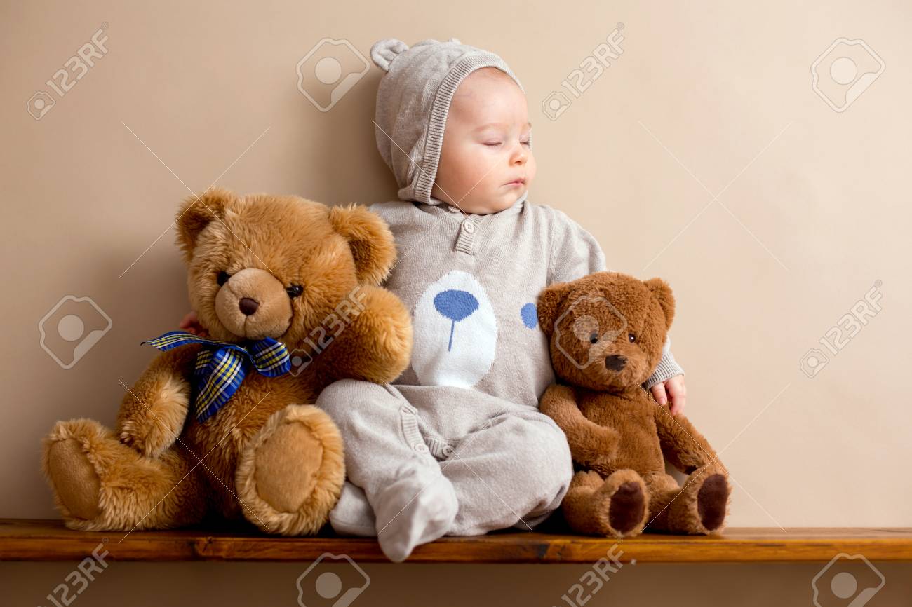 sweet baby boy in bear overall sleeping on a shelf with teddy