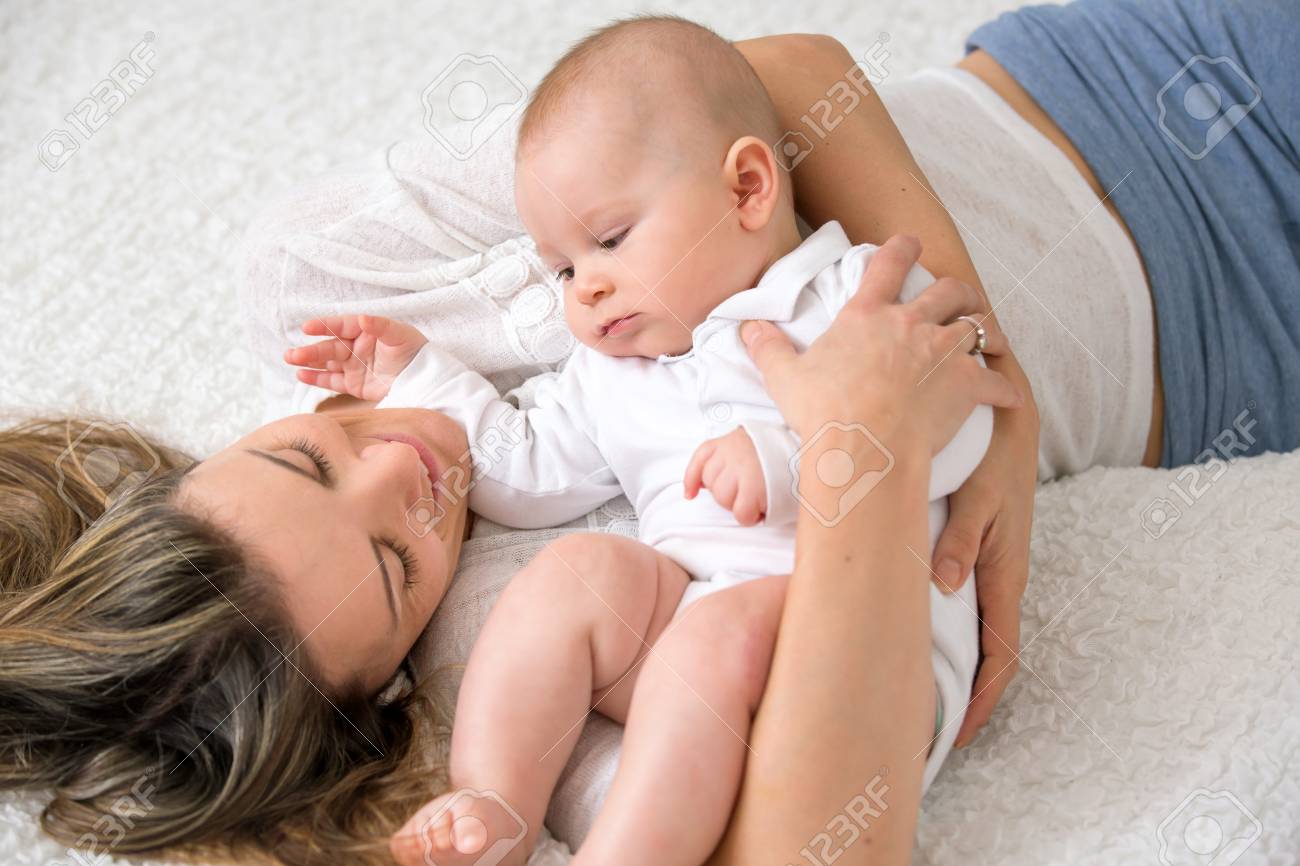 母と彼女の赤ちゃんの息子は笑顔で 大きなベッドで遊んで 彼らの後ろの柔らかいバックライト の写真素材 画像素材 Image