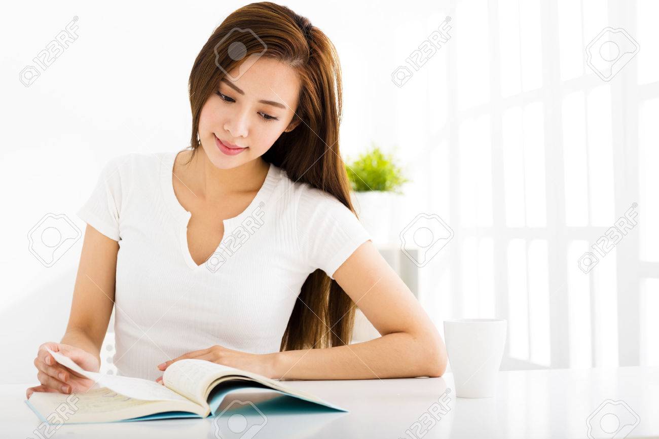 young woman reading a book in living room - 50480588 young woman reading a book in living room - 50480588