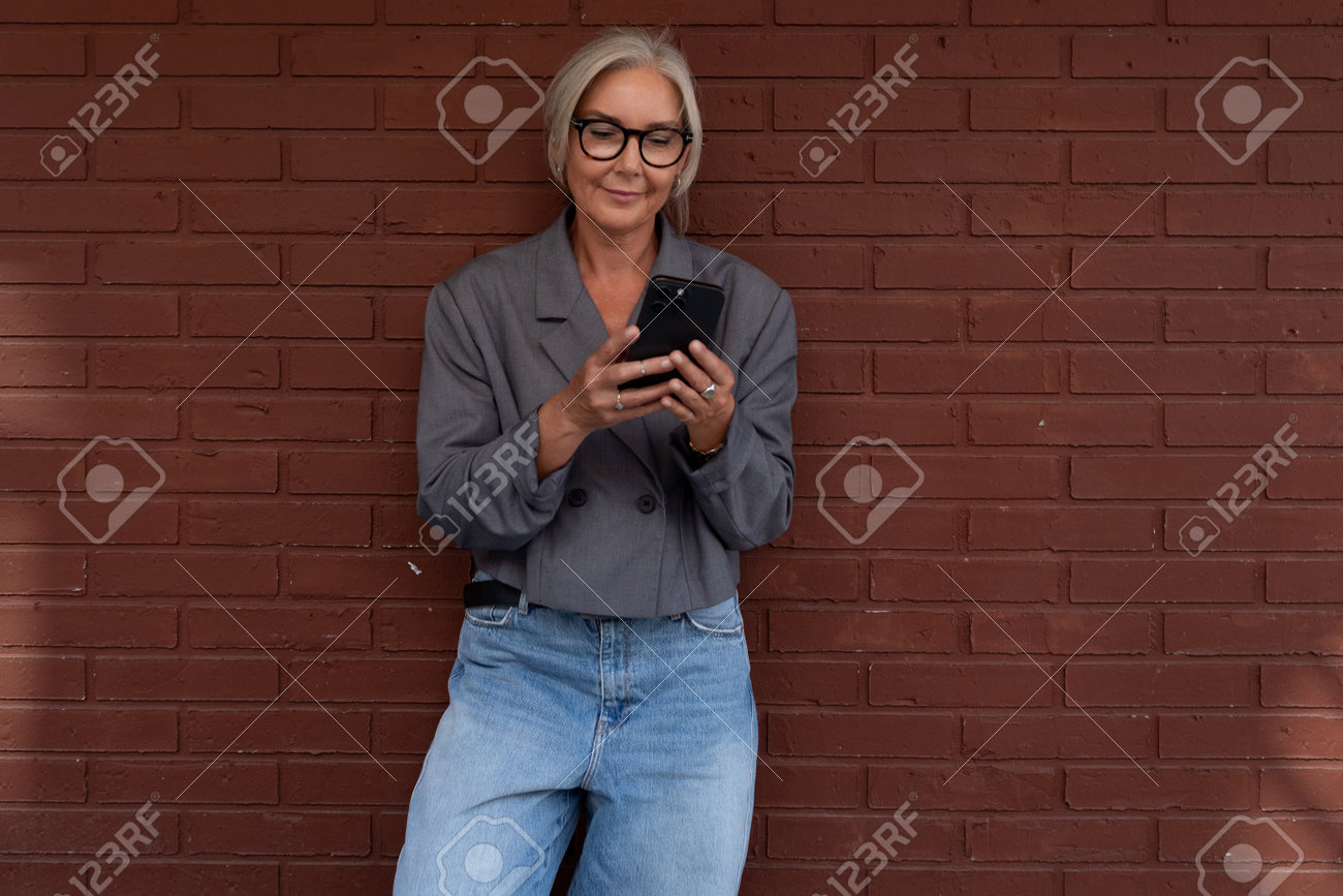 us無料 素人熟女眼鏡画像 グレーのジャケットとジーンズに身を包んだメガネの魅力的なスレンダー熟女がスマートフォンを使用の写真素材・画像素材 Image 212940831