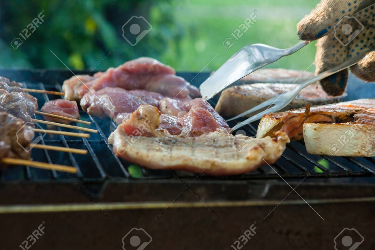 ポータブルバーベキューで肉とケバブの品揃えを焼く男は 彼の手のクローズアップビューでトングのペアでtボーンステーキを持ち上げます の写真素材 画像素材 Image 98204694