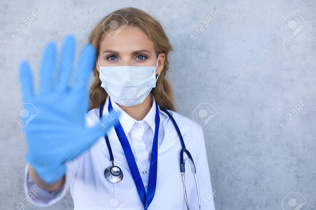 Female doctor in face mask showing stop sign with her hand - 138723082 Female doctor in face mask showing stop sign with her hand - 138723082