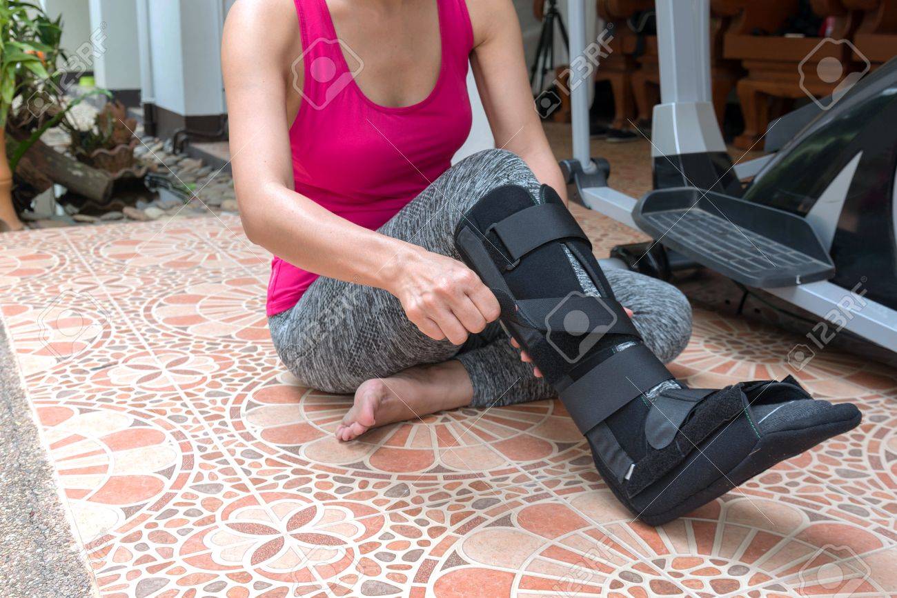 Blessure Femme En Tenue De Sport Avec Attelle Noire Sur La Jambe Assise Sur Le Sol Avec Vélo Dexercice à La Maison Concept Dassurance