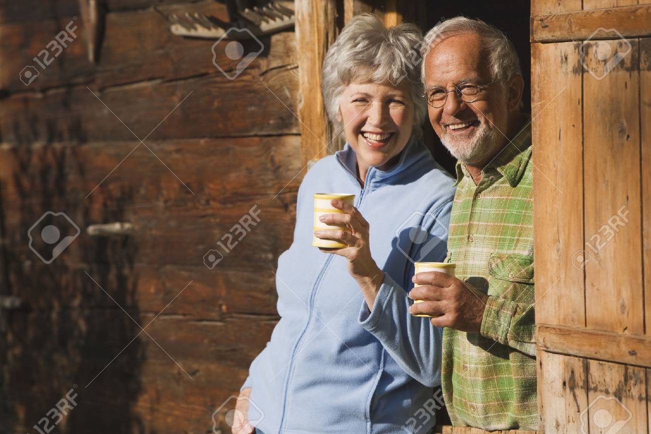 Austria, Karwendel, Senior couple leaning on log cabin's entrance holding mugs - 29823875 Austria, Karwendel, Senior couple leaning on log cabin's entrance holding mugs - 29823875