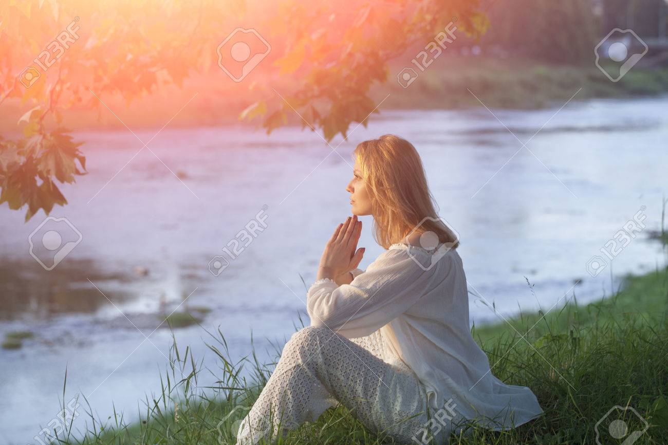 神秘的な自然の夕日背景画像の水平方向の穏やかな川の土手に座っている白い服の若い女性 の写真素材 画像素材 Image
