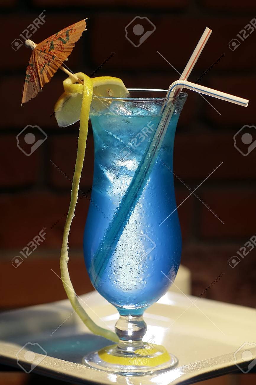 リキュールのブルー キュラソー ウォッカ スプライト黄色レモン柑橘類フルーツと氷のキューブを飲むストローとレンガ背景 垂直写真の上の傘のアルコールの青い珊瑚礁のカクテルを 1 杯 の写真素材 画像素材 Image