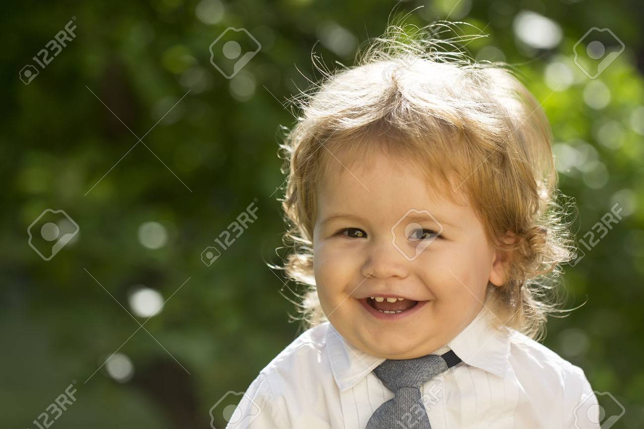 Portrait De Sourire Enfant Garcon Aux Cheveux Boucles Blonds Et Joues Rondes En Chemise Blanche Avec Cravate Regardant Jour Avant Ensoleille Exterieur Sur L Arbre Vert Naturel Feuilles Fond Copyspace Photo Horizontale Banque