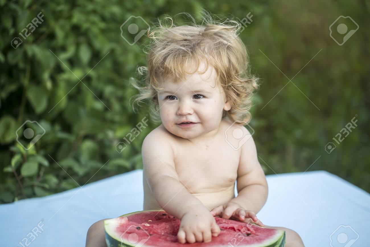 One Small Smiling Boy With Blonde Curly Hair Sitting On Blue Plaid Holding Half Of Fresh