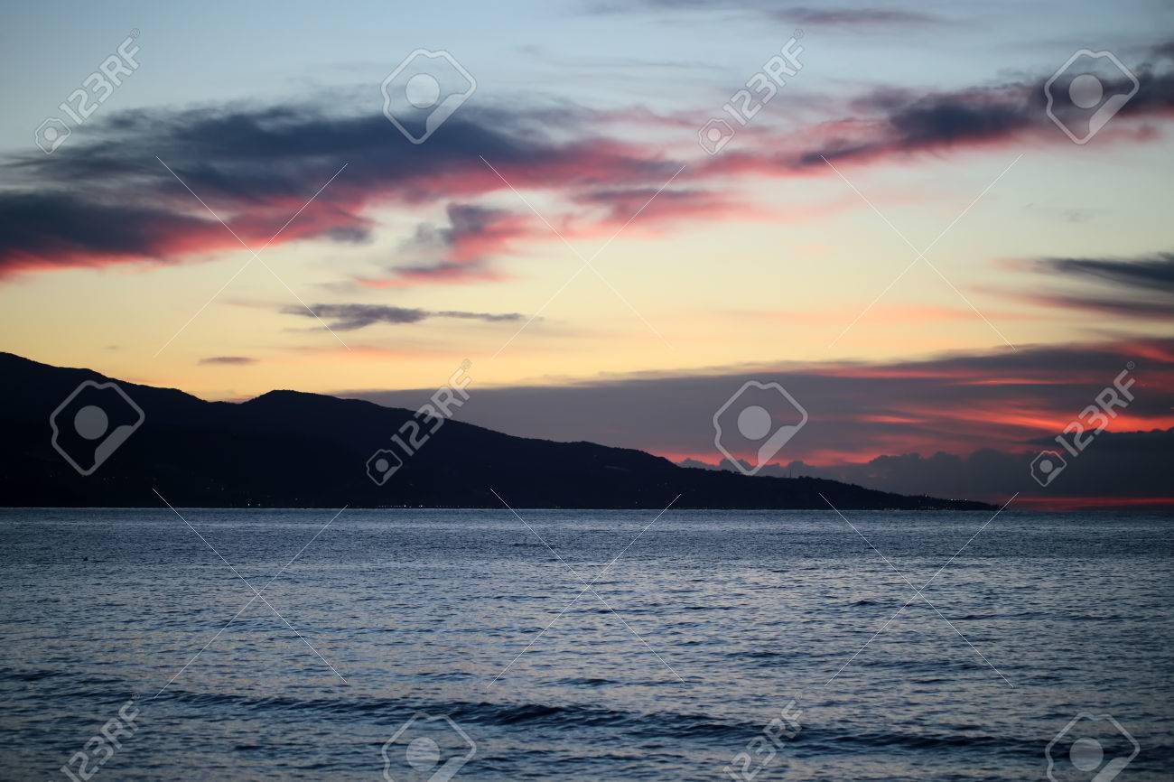明るい暗いと光赤いばら色と青と空の下低い雲のカバー 画像の水平方向の地平線上の夕暮れの暗い山のシルエットを参照してくださいのクローズ アップ穏やかな青い水路海景ビューを夜の魔法 の写真素材 画像素材 Image