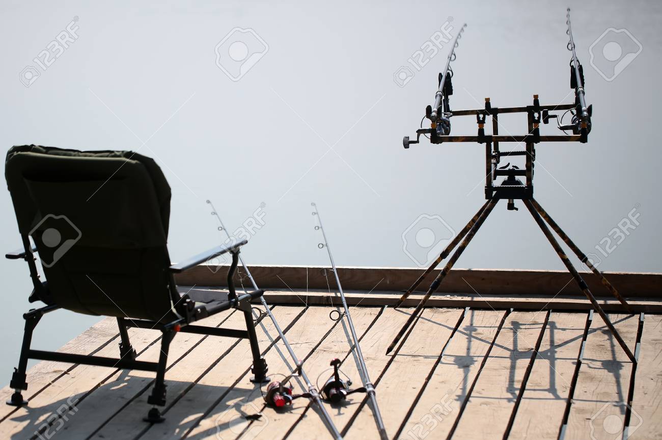 Fauteuil portable pour le repos des cannes à pêche avec des bobines de pose près et de pêche au carbone plaqués sur support debout sur la jetée en Fauteuil portable pour le repos des cannes à pêche avec des bobines de pose près et de pêche au carbone plaqués sur support debout sur la jetée en