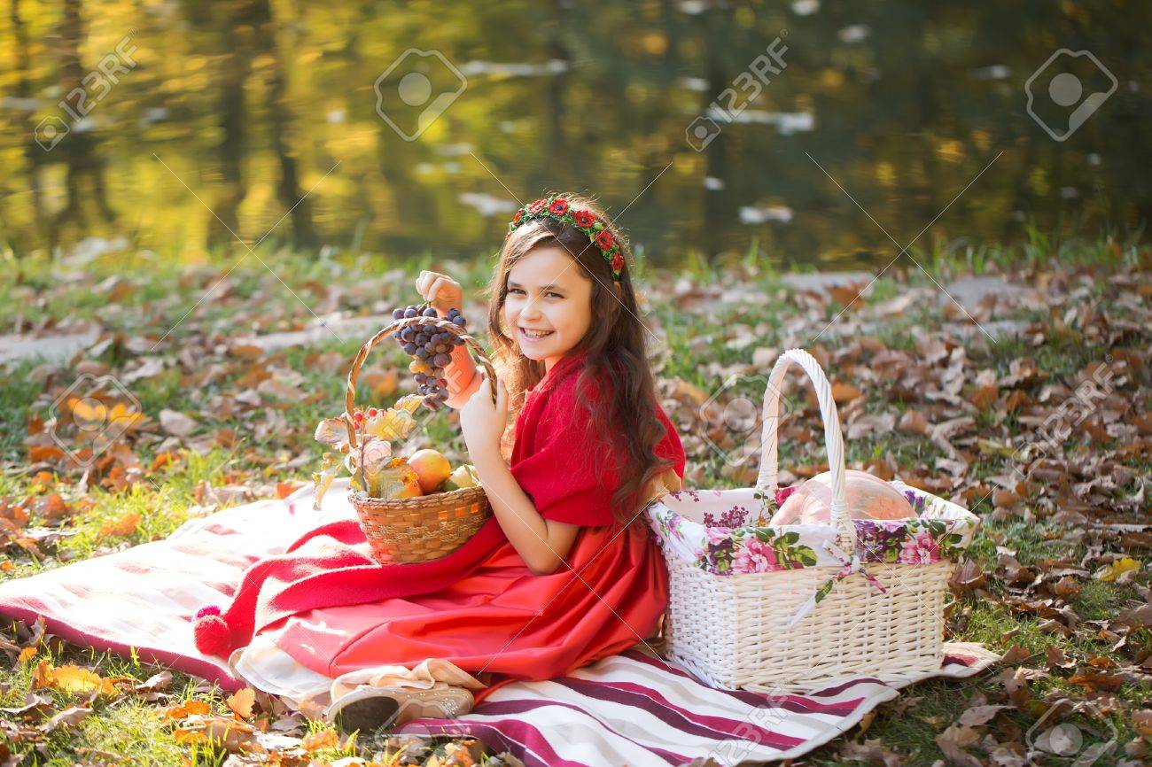 Sourire Petite Fille Dans Des Vêtements Rouges Et Couronne De Fleurs Sur Les Cheveux Noirs Crépus Tenant Bouquet Bleu De Raisin Sur Plaid Avec Des Paniers