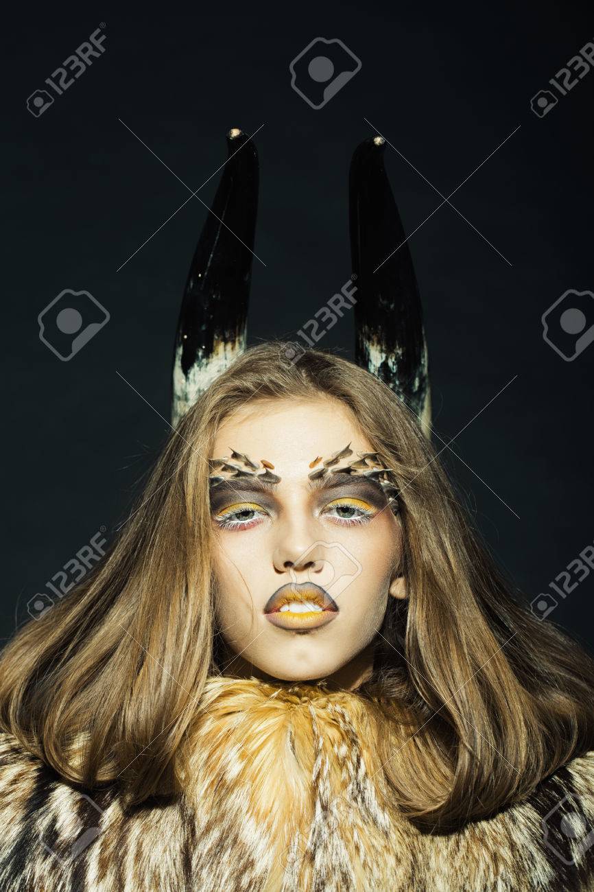 明るい黄金の動物猿メイク顔と黒の背景画像の垂直方向に毛皮のコートの角にトゲがあると 1 つの美しい野生若い女性のポートレート クローズ アップ の写真素材 画像素材 Image