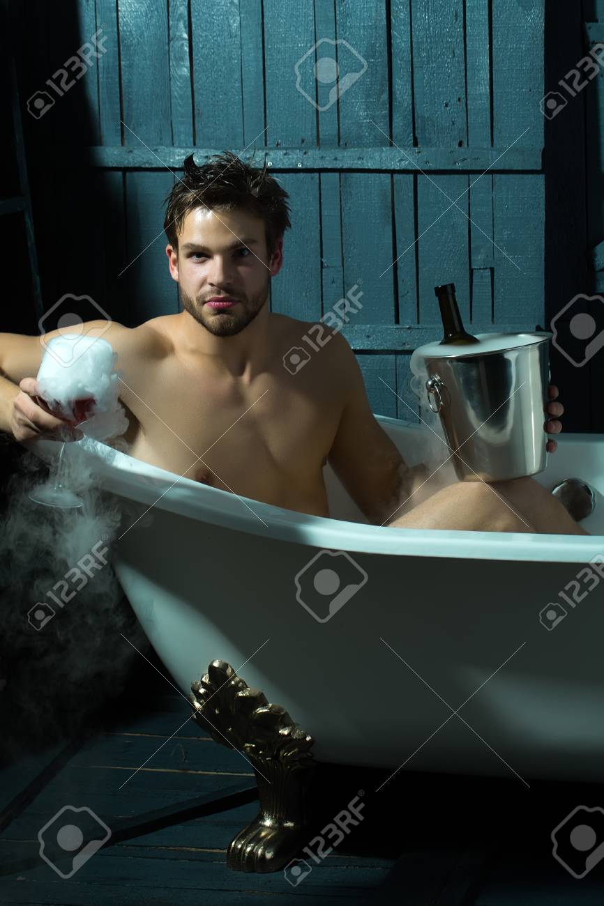 Un Hombre Sensual Muscular Guapo Joven Con Hermoso Cuerpo Desnudo Sentado  En La Tina De Baño Blanco Con Cristal Celebración De Espuma De Humo Luquid  Y Botella En Pila En La Pared