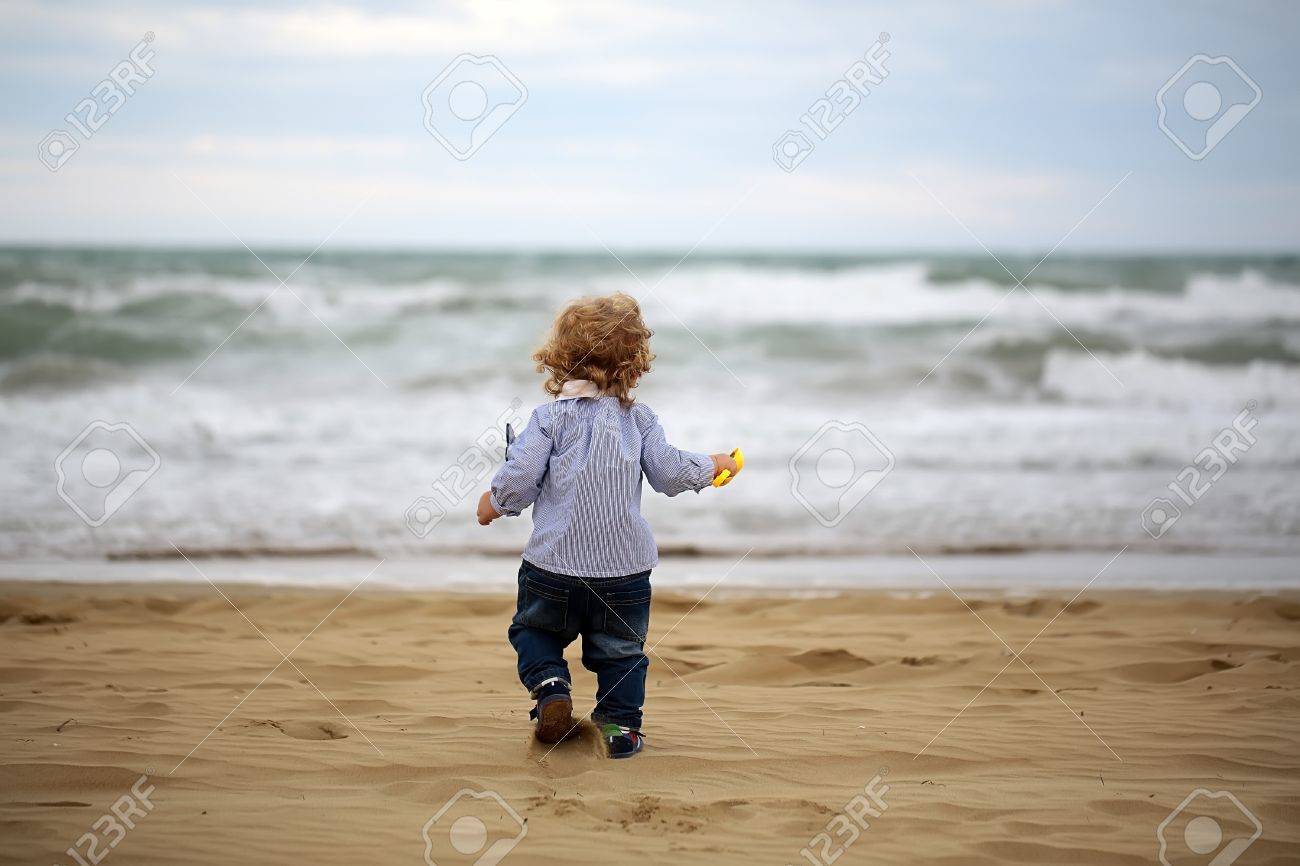 Mignon Blonde Enfant Blonde Minuscule Bebe Enfant Garcon Courir Et Jouer Avec Du Sable Sur La Plage Sur La Morne Journee Sombre Vue Arriere Sur Floue Seascape Fond Image Horizontale Banque D Images