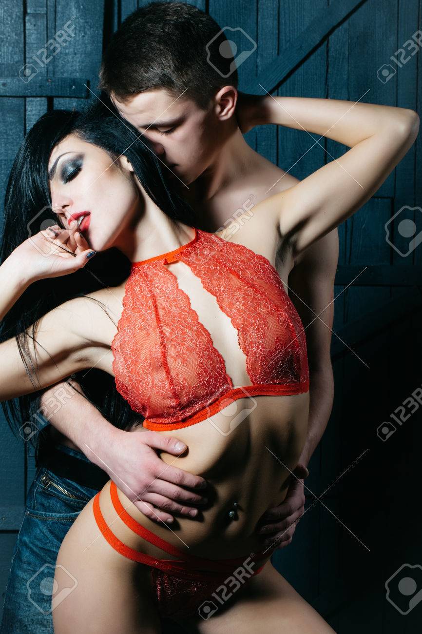 Attractive Young Undressed Brunette Sensual Woman With Beautiful Straight Body In Red Lace Lingerie With Muscular Man Posing Indoor On Wooden Background, Vertical Picture Stock Photo, Picture And Royalty Free Image