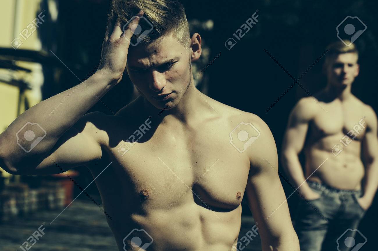 Modelo Del Hombre Se Desnudó Con Un Fuerte Cuerpo Musculoso Arregla El Pelo  En Primer Plano, Mientras Culturista Hermano Gemelo Con El Pecho Desnudo  Plantea Al Aire Libre En El Fondo Paisaje
