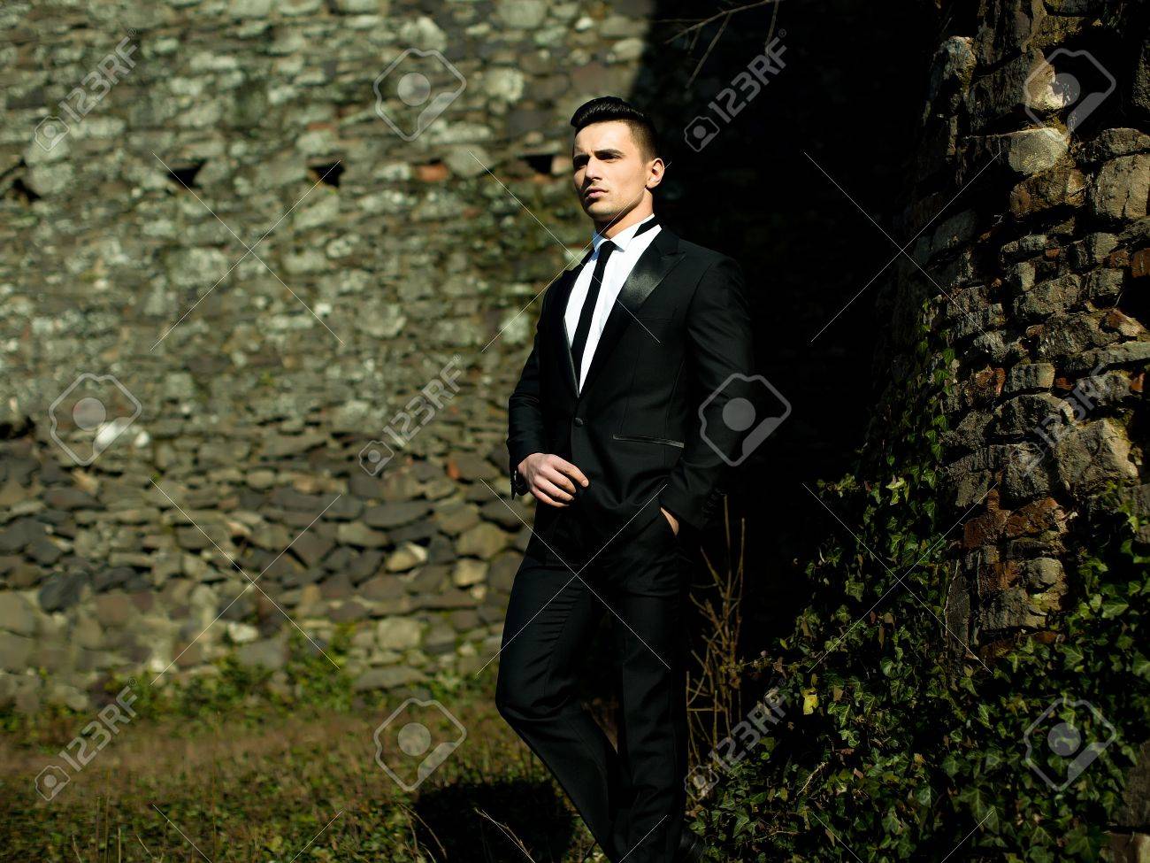 男は半分顔細いネクタイ ポーズでスーツのズボンのポケット 1 つ足の後方で手でハンサムなエレガントなモデルは若い石工の背景に屋外 の写真素材 画像素材 Image