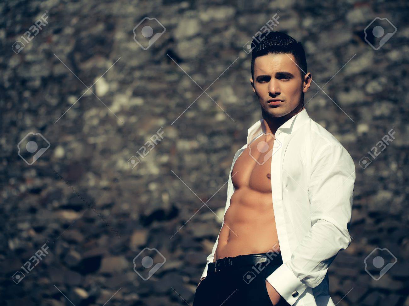 El Hombre Con El Torso Desnudo Joven Modelo Sensual En La Camisa Blanca Se  Abría Posturas Abiertas Con Las Manos En Los Bolsillos Del Pantalón Negra  Afuera En El Fondo De Mampostería