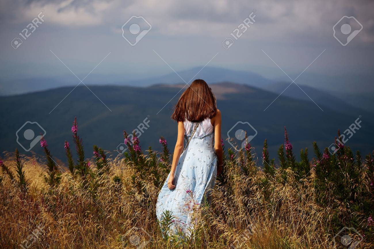 Pretty cute brunette woman or girl stands back in blue dress waving on wind outdoor on beautiful landscape - 64743602 Pretty cute brunette woman or girl stands back in blue dress waving on wind outdoor on beautiful landscape - 64743602