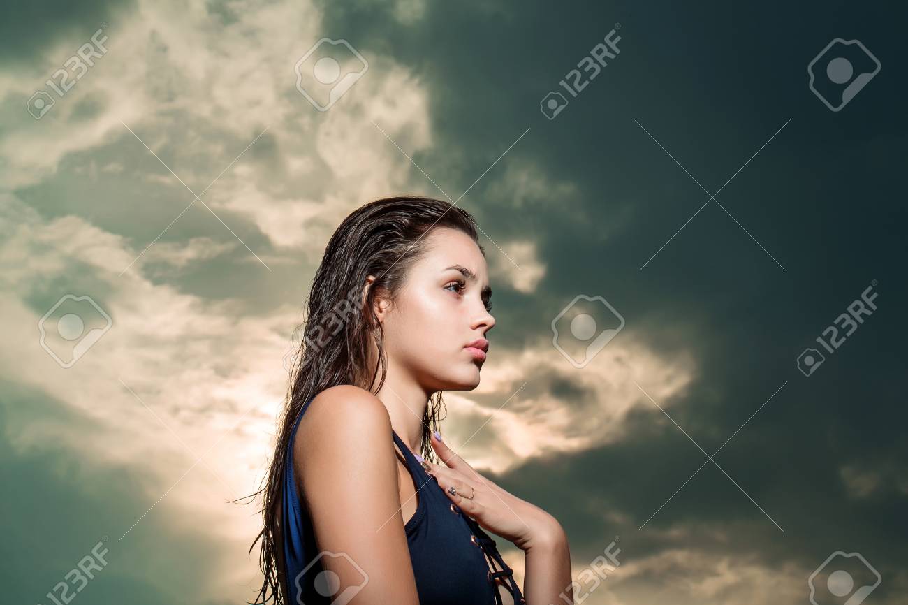 若い可愛い女性やかわいいセクシーな顔とスリム フィット体空を背景に屋外でポーズ ブルー水着で濡れた長いブルネットの髪を持つ少女 の写真素材 画像素材 Image