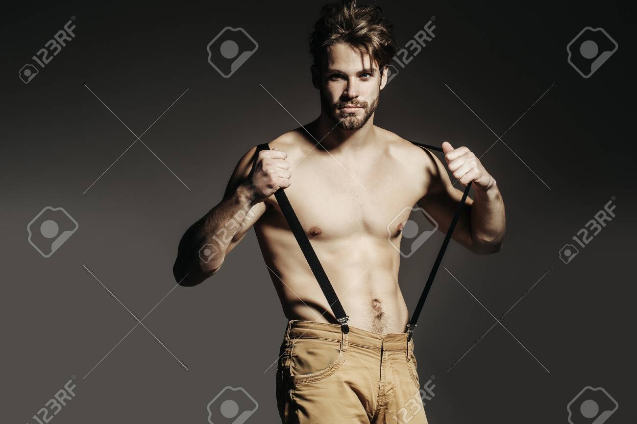 パンツにサスペンダーでハンサムな男ファッション セクシーな若いアゴヒゲ マッチョ モデルは 灰色の背景の裸筋肉胴を保持 の写真素材 画像素材 Image