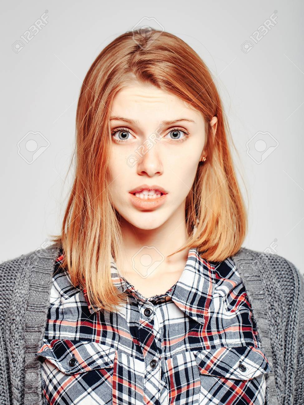 びっくりしたきれいな女の子や格子縞のシャツと灰色の背景にニット コートしわ額にブロンドの髪でかわいい美人女性モデル の写真素材 画像素材 Image