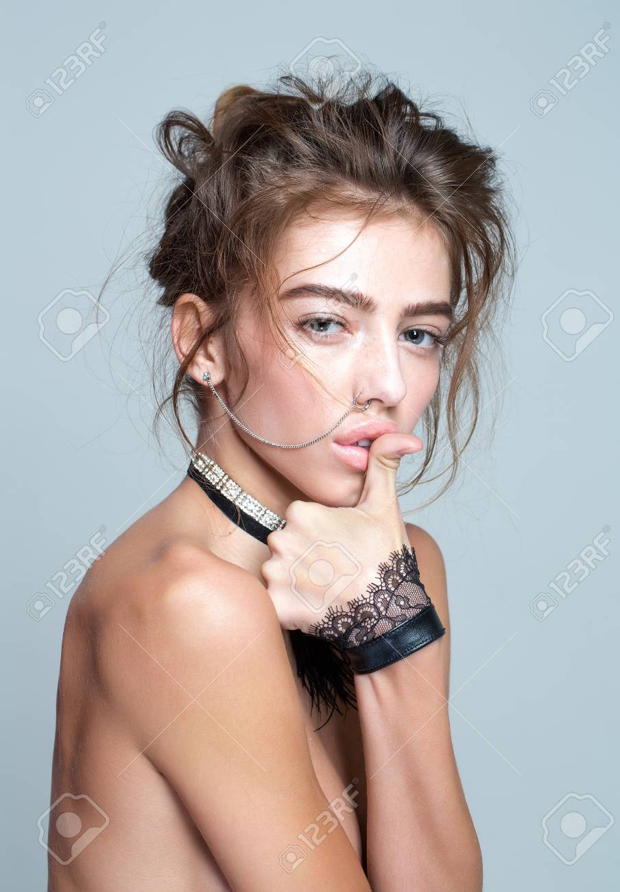 Pretty Girl Or Beautiful Woman, Young, Cute, Sexy, Fashion Model With Curly  Hair, Nose Ring And Necklace With Cuffs Poses Topless With Thumb On Lips On  Grey Background Фотография, картинки, изображения и