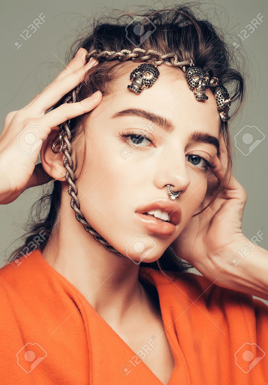 かわいい女の子や美人 若い かわいい セクシーなファッションモデル灰色の背景にオレンジ色のコートで顔に頭蓋骨に金属チェーンの巻き髪と鼻リング ポーズ の写真素材 画像素材 Image