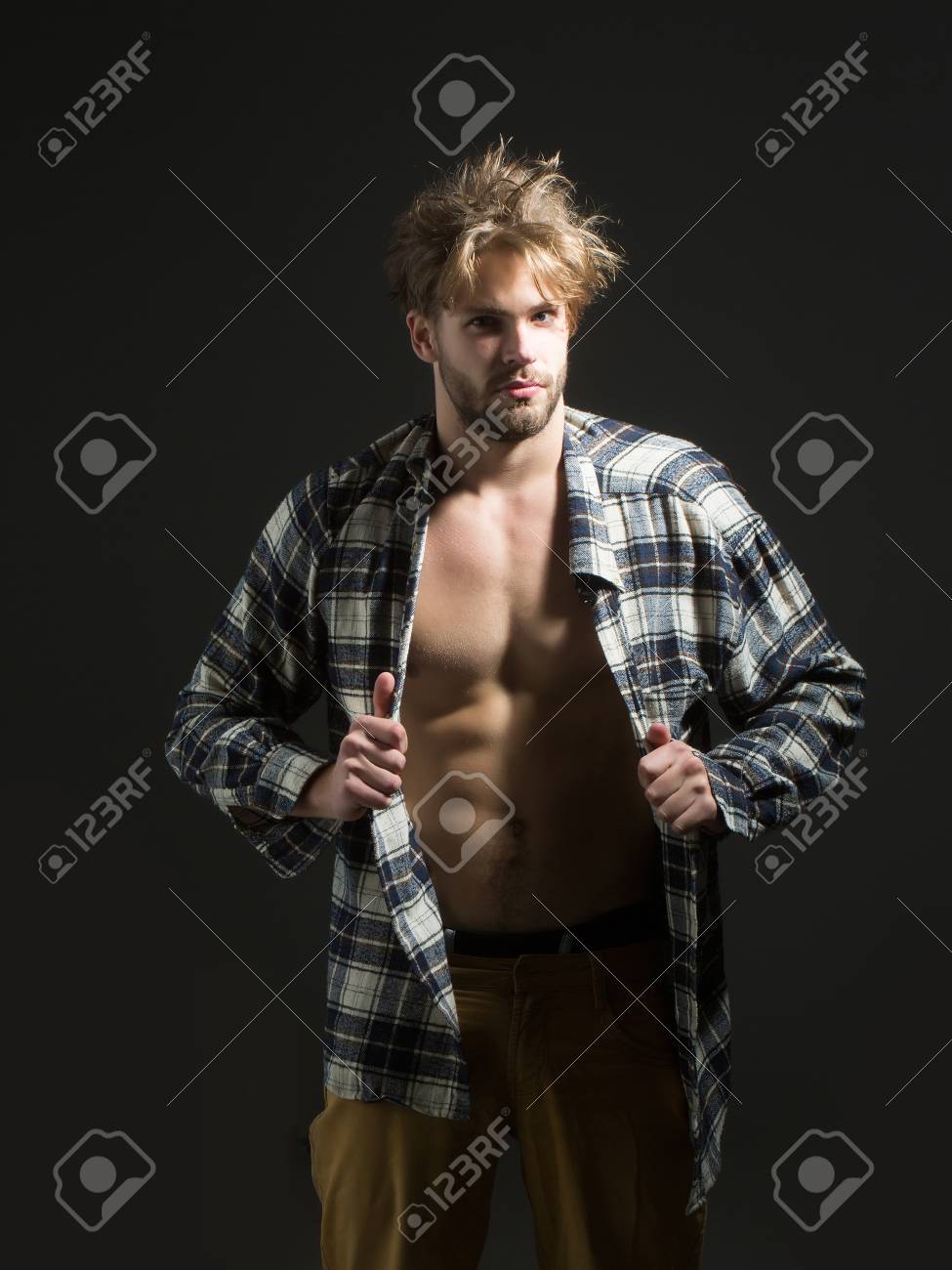ハネた髪のベージュ パンツの若い男は暗い背景に彼の格子縞のシャツを脱ぐ の写真素材 画像素材 Image