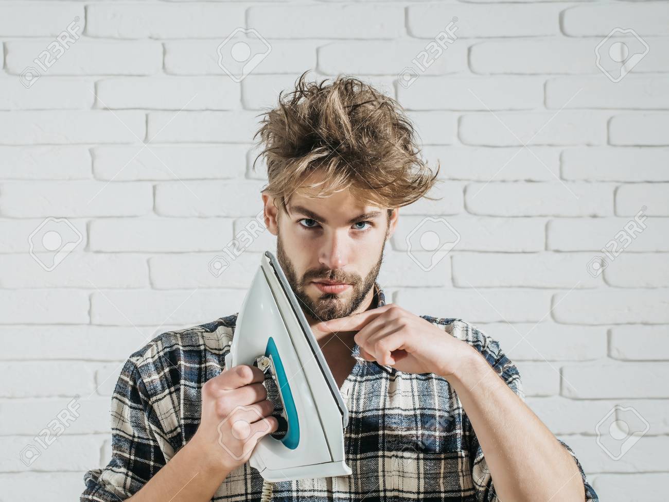 Young Handsome Man In Stylish Plaid Shirt Touches White Iron
